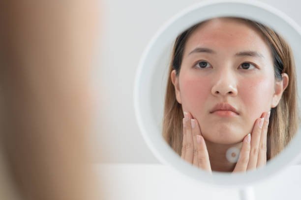 woman checking skin for redness and irritation in mirror after applying expired skincare