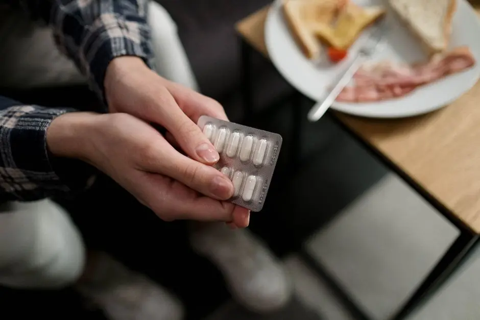 Close-up of a person holding a blister pack of pills with breakfast in the background, indicating medication and daily routine.
