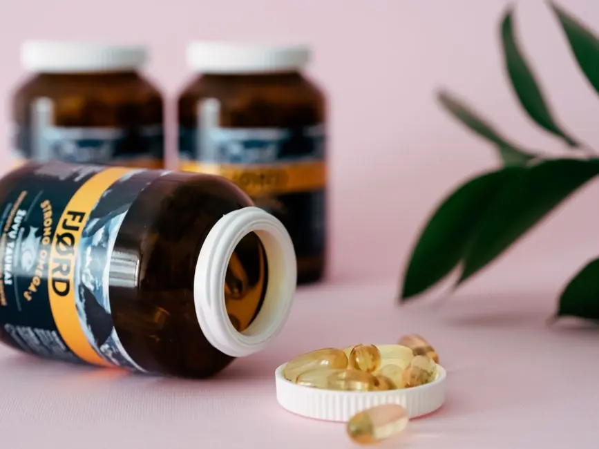 Close-up of omega-3 capsules and bottles on a pink background, ideal for health and wellness themes.