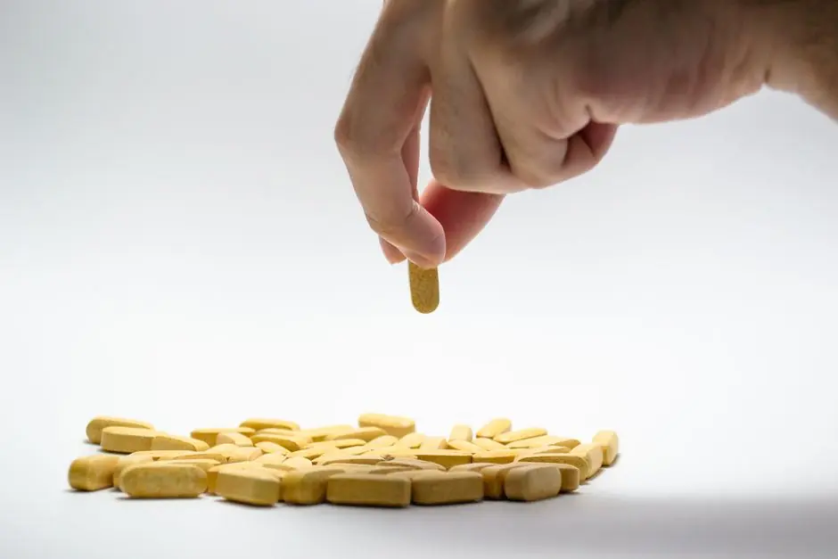 Close-up of a hand picking a yellow pill from a pile of tablets on a white surface.