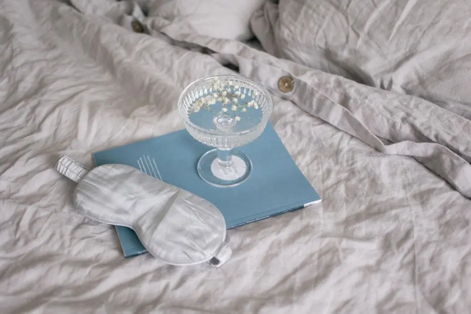 A relaxing setup with a sleep mask, book, and glass flowers on a bed.