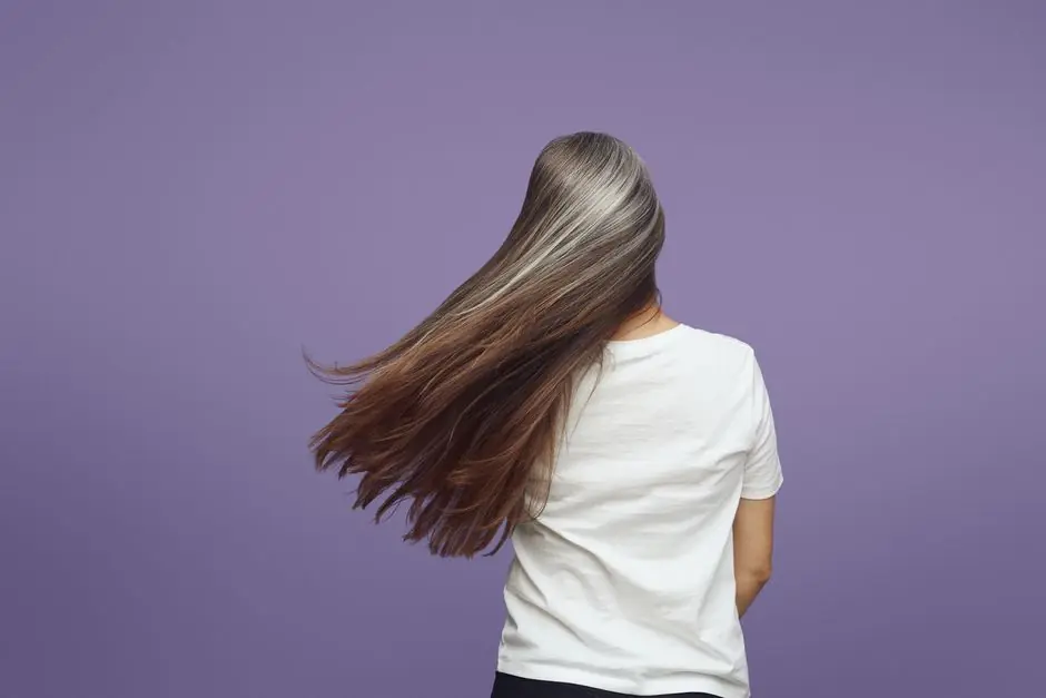 Rear view of a woman with long, flowing gray hair against a purple backdrop.